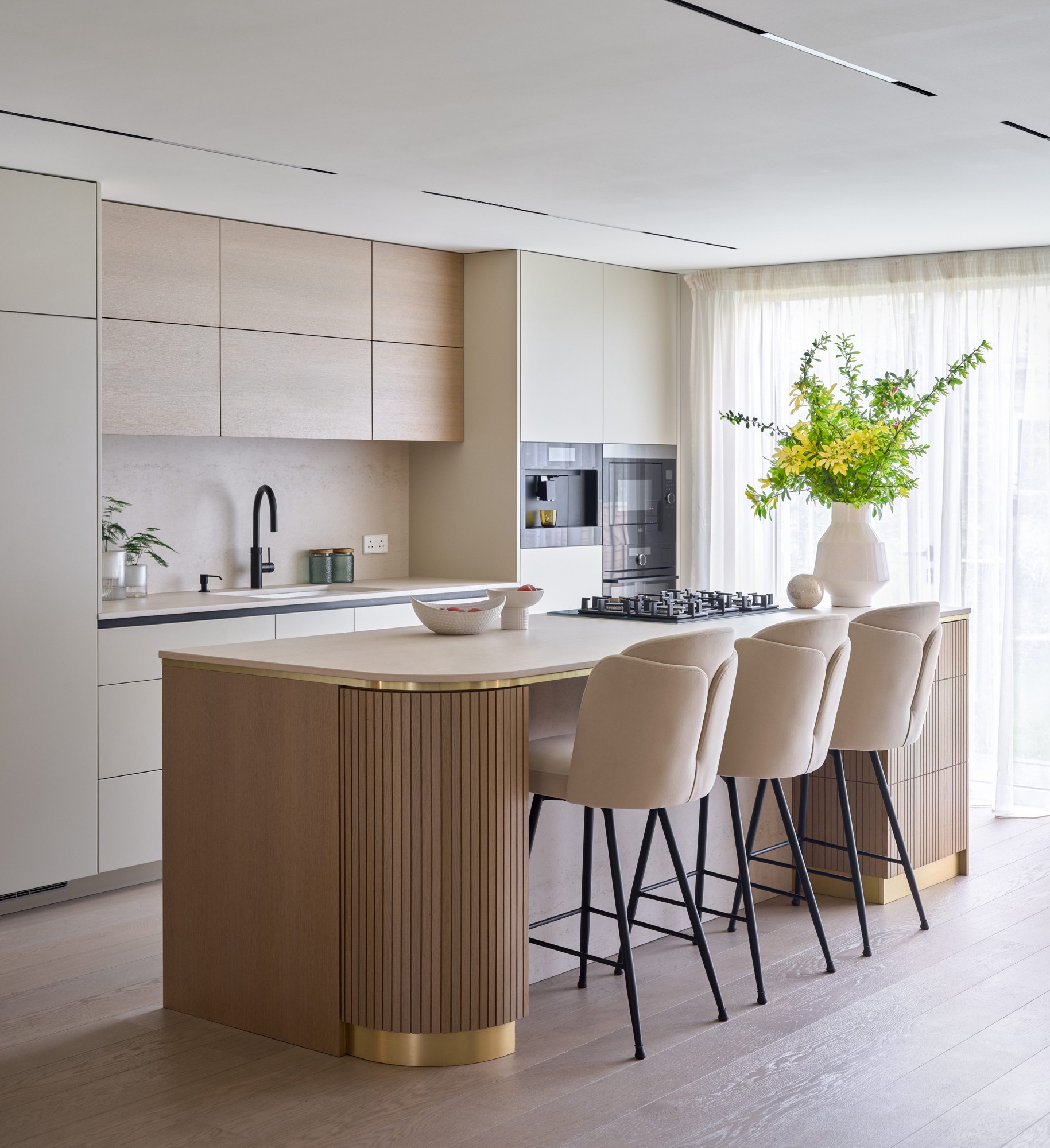 Contemporary kitchen with fluted oak island, brass detailing and upholstered bar stools, designed by Studio 32