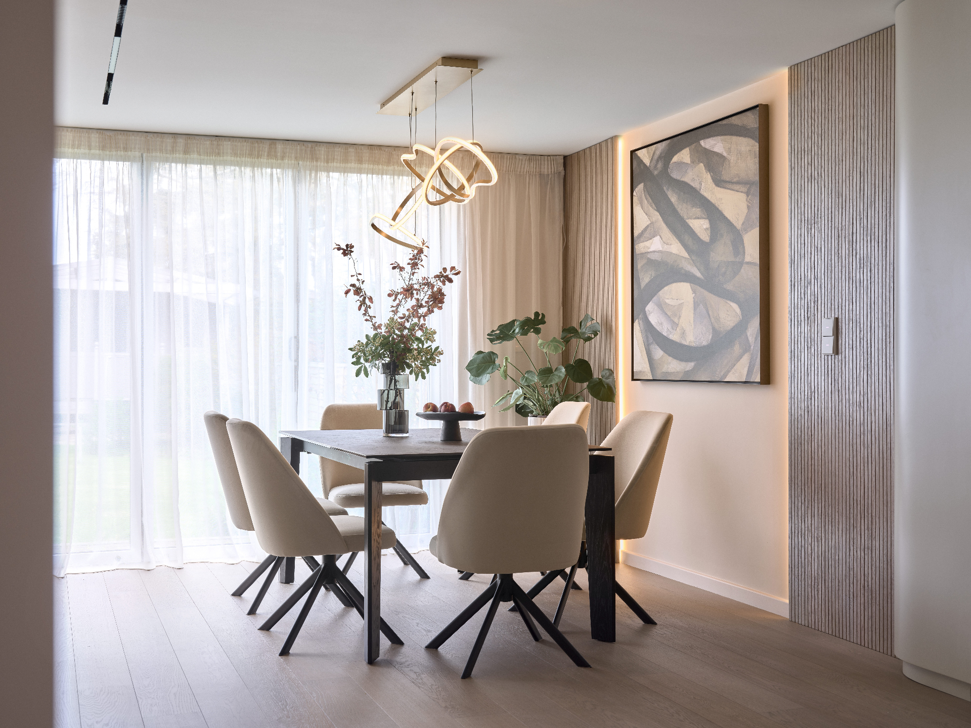 Contemporary dining room with a neutral palette, upholstered chairs, sculptural pendant light, abstract wall art and soft sheer curtains.